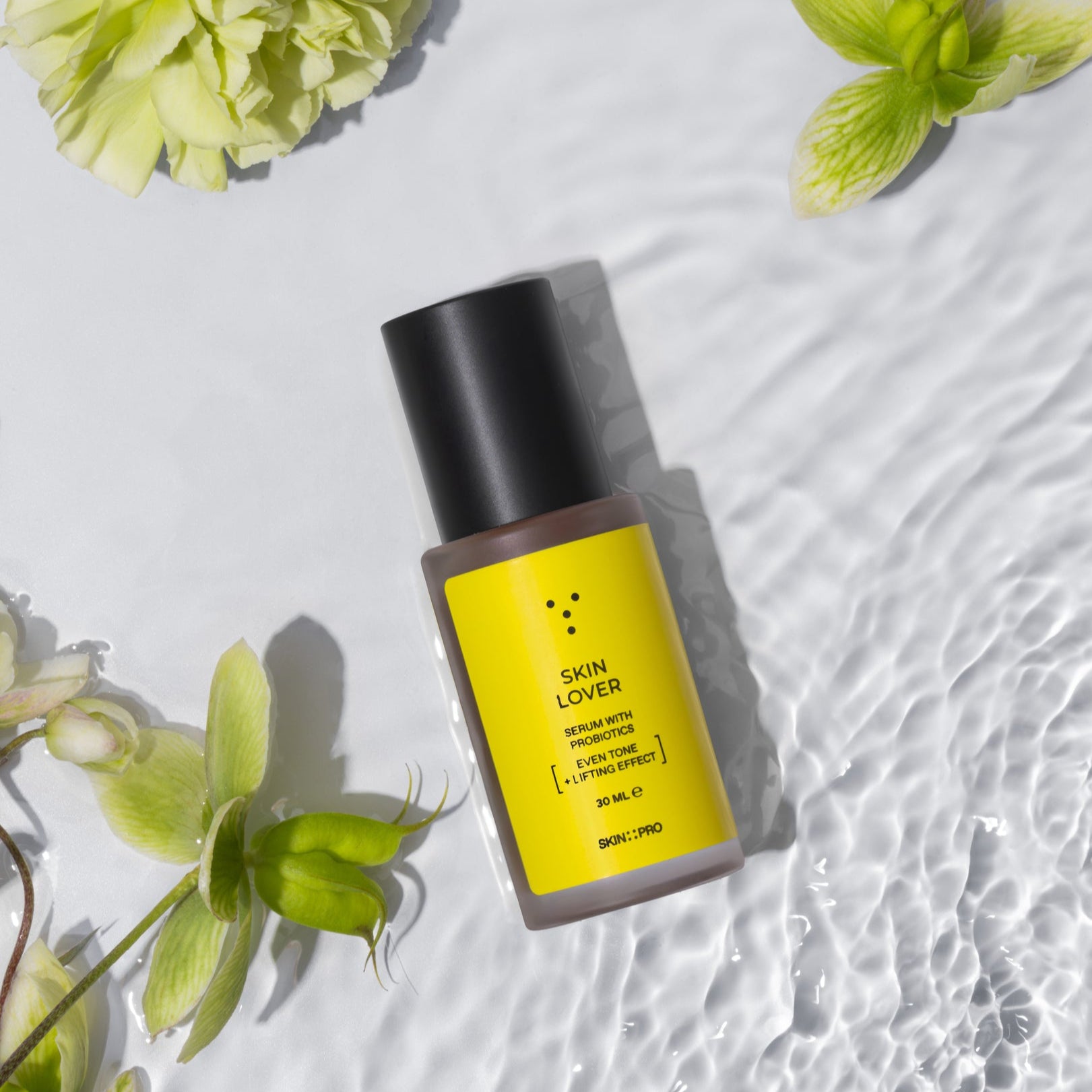 Skincare bottle with yellow label and black cap on a textured white surface with green flowers.